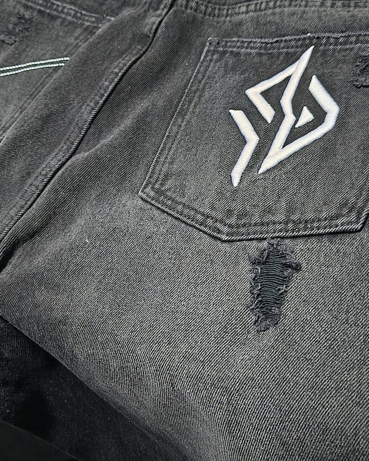 SUÐR Denim Washed Black – Rückansicht mit Emblem und Riss, von SUÐR