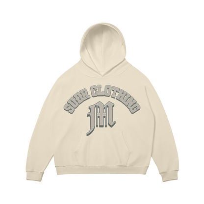 SUÐR M Hoodie – Hoodie in Rice Apricot, Vorderseite mit SUÐR CLOTHING im Bogen, darunter das M in Blackletter über der Kängurutasche, Emblem und SUÐR-Schriftzug auf den Ärmeln, liegend