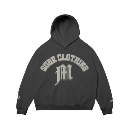 SUÐR M Hoodie – Hoodie in Black, Vorderseite mit SUÐR CLOTHING im Bogen, darunter das M in Blackletter über der Kängurutasche, Emblem und SUÐR-Schriftzug auf den Ärmeln, liegend